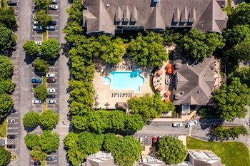 An aerial view of a parking lot with a swimming pool and trees.